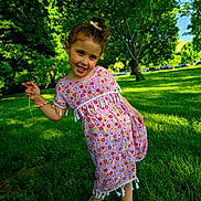 Maria joined the competition — help win amazing prizes! child, girl, toddler, smiling, portrait, outdoor, park, garden, grass, trees, sunlight, summer, dress, floral_pattern, hair_bow, bracelet, shoes, standing, leaning, flower
