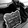 baby, child, black_and_white, chalkboard, hat, wooden_steps, sign, clothing, sitting, footwear, portrait, infant, outdoor, milestone, cute, expression, person, flooring, decor, monochrome