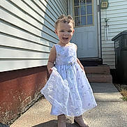 Nylah is registered to the contest to win money with this photo: boots, child, concrete, curly_hair, daylight, door, dress, flower_pattern, happy, house, outdoor, person, side_view, sidewalk, smiling, steps, sunlight, toddler, wall, white_dress