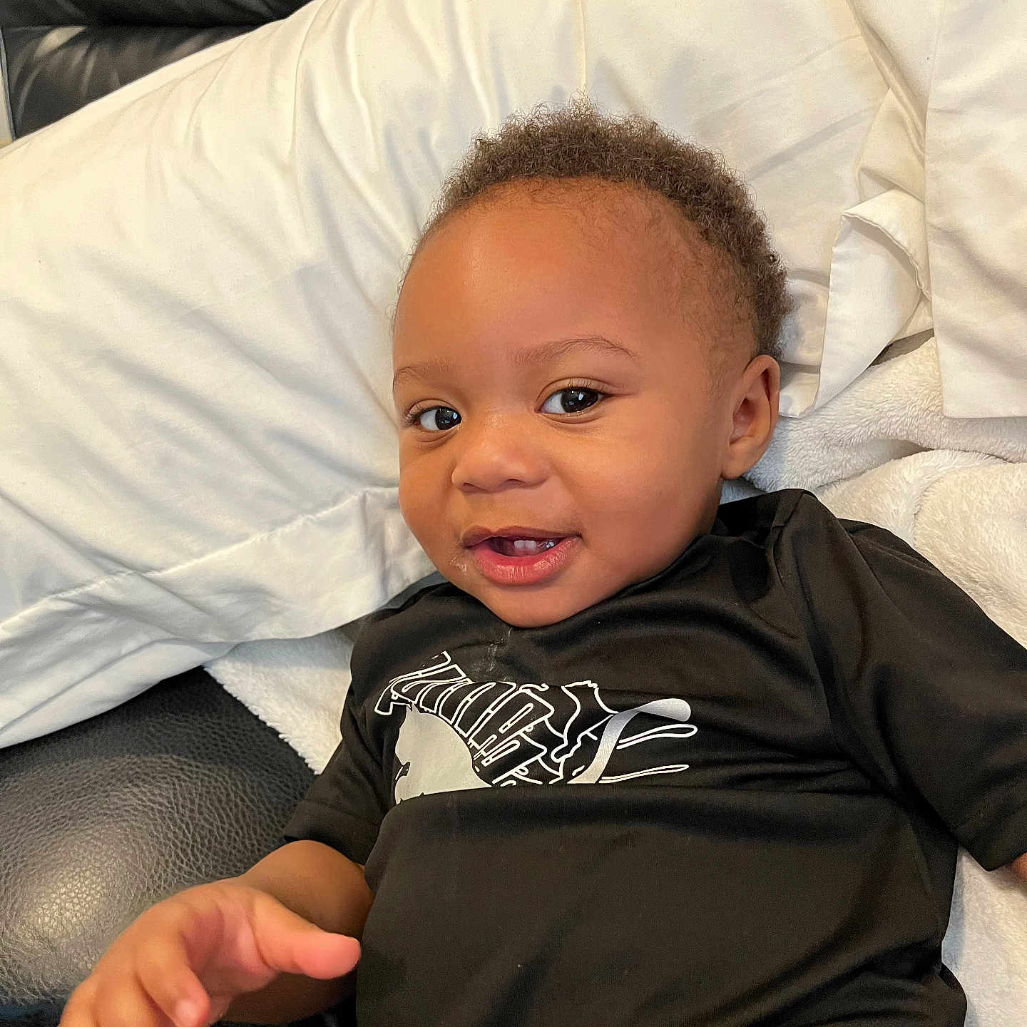 Dnero is registered to the contest to win money with this photo: toddler, child, smiling, black_shirt, couch, pillow, blanket, hand, face, happy, indoors, curly_hair, skin, portrait, person, seated, cute, baby, comfortable, cozy