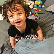 Asher is registered to the contest to win money with this photo: toddler, child, curly_hair, blue_eyes, bed, blanket, toy, smile, indoor, person, happy, climbing, cute, infant, playful, pajamas, furniture, home, portrait, baby