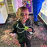 Kingston is registered to the contest to win money with this photo: child, smiling, toy, dinosaur, arcade, game, carpet, colorful, indoor, person, jacket, shoes, happy, play, lighting, casual_clothing, hand, adult, floor, background