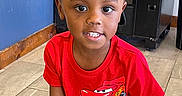 Kingston is registered to the contest to win money with this photo: child, boy, red_tshirt, cartoon, indoor, bench, vending_machine, floor_tile, smiling, portrait, short_hair, casual_clothing, young, person, bright_colors, seated, background, wall, happy, eyes