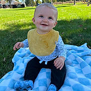Noah joined the competition — help win amazing prizes! baby, child, smiling, sitting, outdoors, park, backyard, grass, blanket, yellow_bib, long_sleeves, black_pants, blue_socks, infant, portrait, sunlight, gazebo, playground, trees, happy