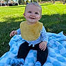 baby, child, smiling, sitting, outdoors, park, backyard, grass, blanket, yellow_bib, long_sleeves, black_pants, blue_socks, infant, portrait, sunlight, gazebo, playground, trees, happy