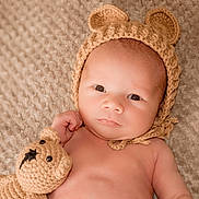 Jacek is registered to the contest to win money with this photo: baby, infant, knitted_hat, bear_ears, crocheted_toy, teddy_bear, blanket, soft_texture, cute, portrait, child, newborn, relaxed, indoors, closeup, skin, lying_down, hand, expression, warm_colors