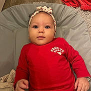 Nélïa participe au concours pour gagner de l'argent avec cette photo : baby, infant, headband, red_shirt, lying_down, blanket, cushion, hand, floor, wooden_floor, curious, indoors, person, child, portrait, cute, face, clothing, soft_texture, warm_colors
