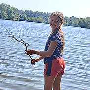 Amy a rejoint le concours — aidez-le/la à gagner de superbes lots ! child, girl, lake, water, stick, smile, outdoor, nature, trees, braid, shorts, tshirt, sunny, summer, recreation, playing, happy, standing, shore, reflection