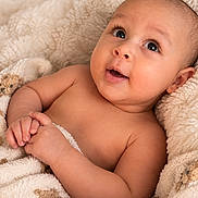 Nagi is registered to the contest to win money with this photo: baby, infant, child, portrait, smiling, happy, lying_down, blanket, teddy_bear, cozy, indoors, close_up, face, eyes, hands, bare_arms, brown_skin, soft_lighting, nursery, adorable
