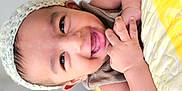 Alzaan is registered to the contest to win money with this photo: baby, smiling, child, knitted_cap, quilt, yellow, white, bed, pillow, happy, face, infant, cute, indoors, portrait, skin, hand, lying, closeup, soft_light