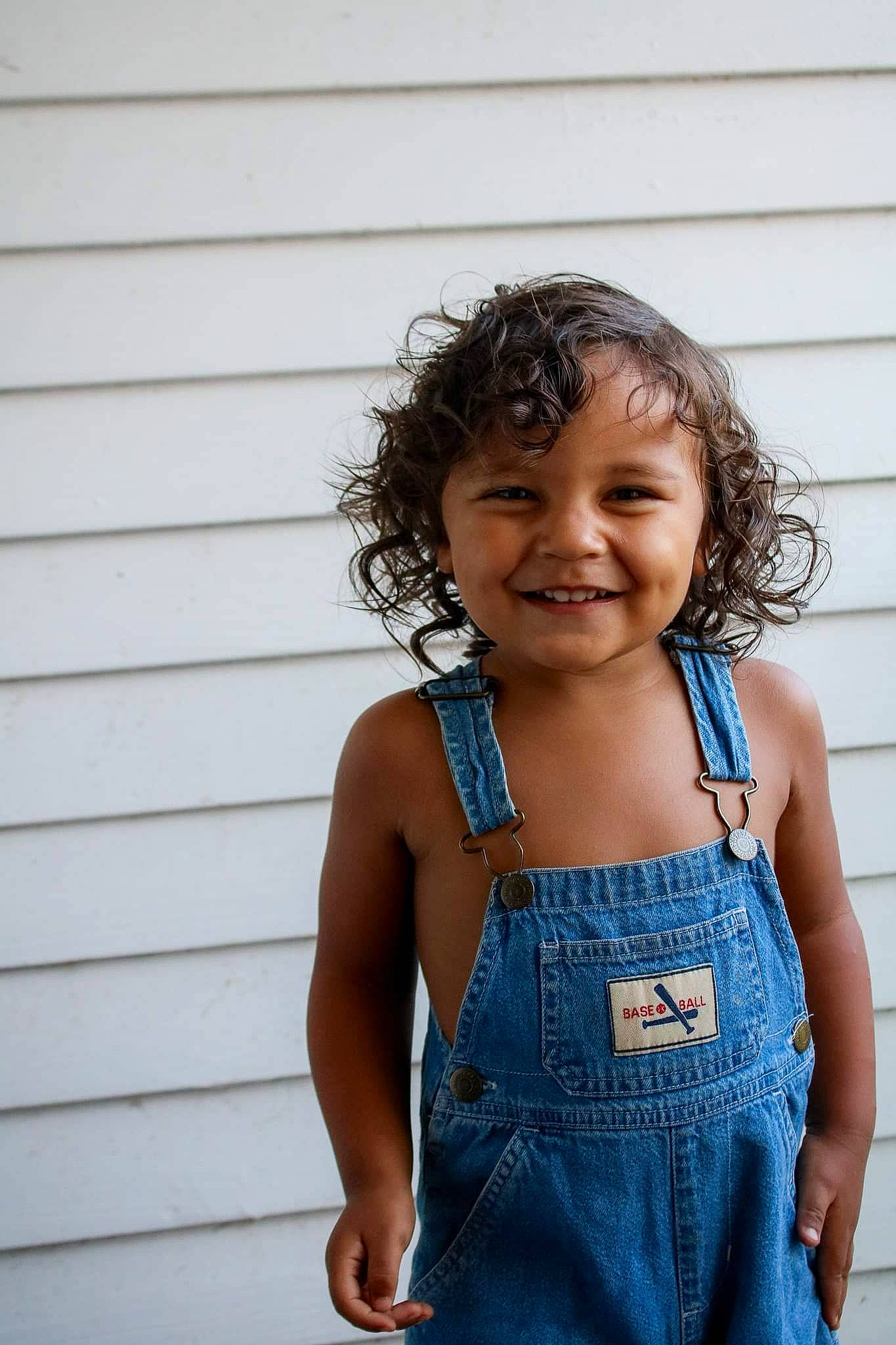 Prince is registered to the contest to win money with this photo: abdomen, blue, child, child_model, denim, facial_expression, happy, jeans, joy, overall, person, shoulder, sleeveless_shirt, smile, standing, textile, toddler, trunk, vacation, waist