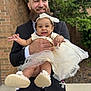 Kylani joined the competition — help win amazing prizes! baby, beard, brick_wall, celebration, child, dress, family, footwear, formal_wear, greenery, happy, headband, holding, man, outdoor, pacifier, person, portrait, smiling, tulle_skirt