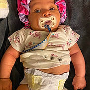 Kylani is registered to the contest to win money with this photo: baby, bonnet, child, clothing, cute, diaper, expression, fist, floral_pattern, indoor, infant, lying_down, newborn, pacifier, person, pink, purple, skin, small_hands, towel