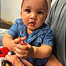 baby, child, denim_shirt, pink_headband, toy_car, hand, face, person, cute, indoor, expression, curious, skin, eye, infant, holding, adult_hand, seated, clothing, portrait