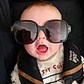 baby, child, sunglasses, car_seat, seat_belt, open_mouth, striped_shirt, face, head, infant, cute, black, clothing, safety, expression, person, portrait, young, accessory, close_up