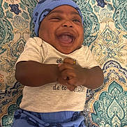Khazir joined the competition — help win amazing prizes! baby, infant, laughing, smiling, blue_hat, blue_pants, clothing, patterned_blanket, happy, joyful, cute, lying_down, hands_clasped, portrait, child, indoors, fabric, text_on_clothing, close_up, human