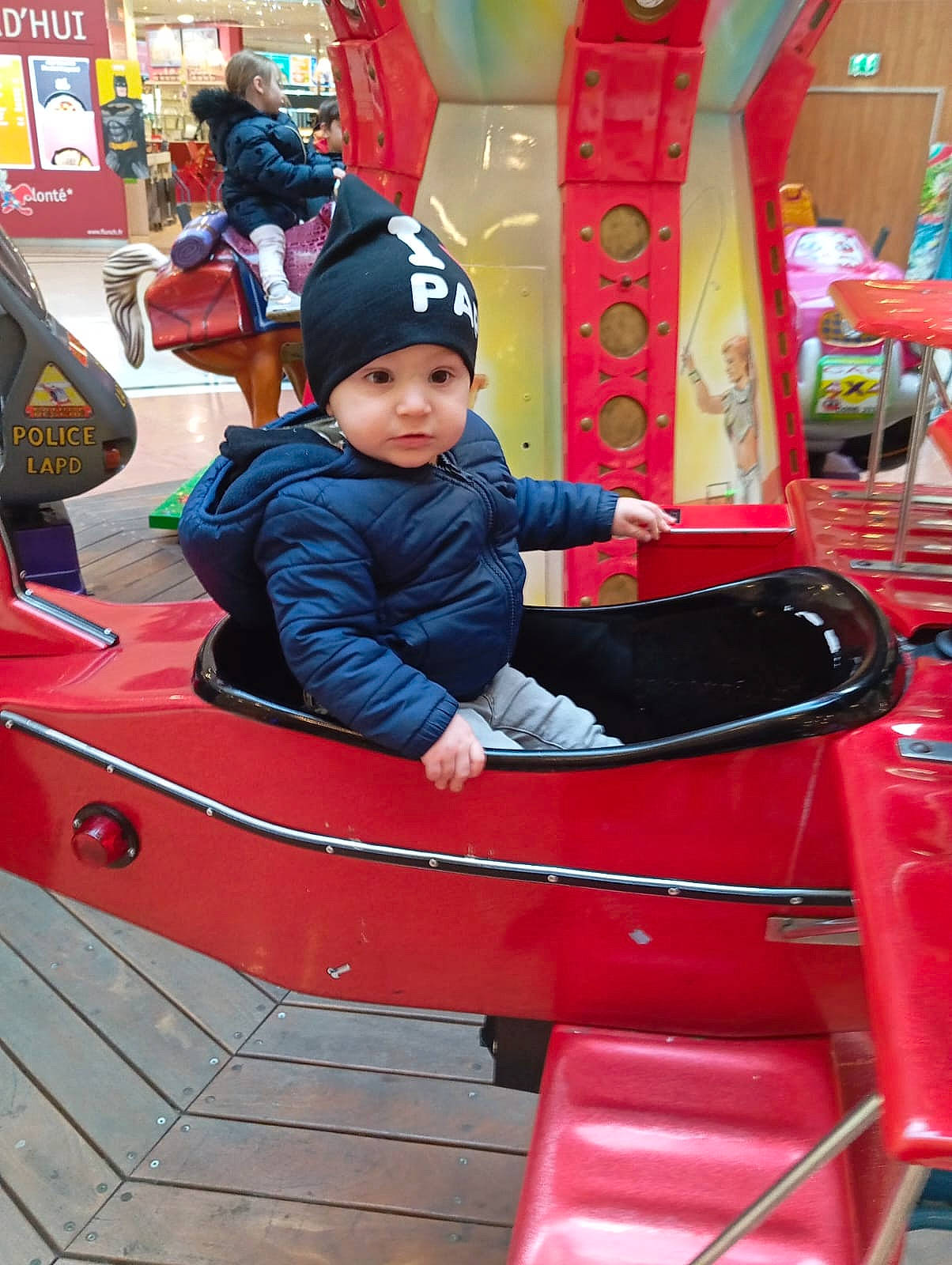 Arthur a rejoint le concours — aidez-le/la à gagner de superbes lots ! amusement_ride, automotive_exterior, baby_toddler_clothing, baseball_cap, cap, child, fun, headwear, jacket, leisure, magenta, motor_vehicle, nonbuilding_structure, outdoor_recreation, person, play, playground, recreation, red, sitting