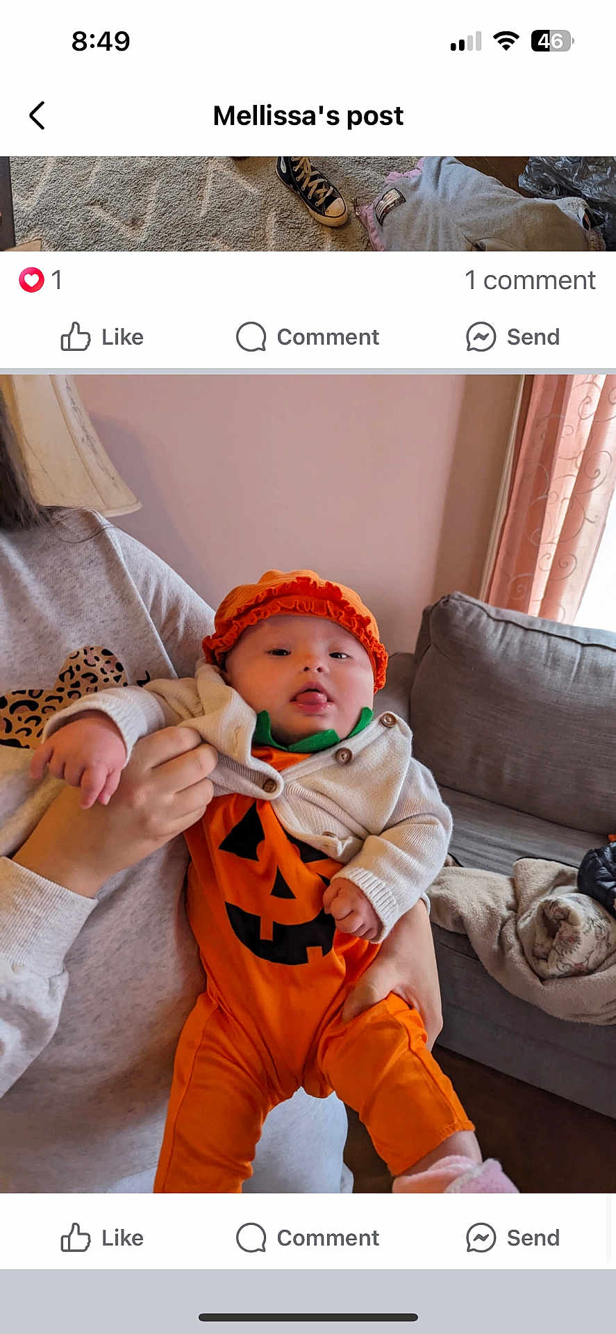 Alana is registered to the contest to win money with this photo: baby, infant, pumpkin_costume, orange_clothing, hat, tongue_out, holding, person, sweatshirt, leopard_print, couch, blanket, living_room, curtains, window, hand, face, cute, indoor, cozy