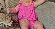 Jaclyn is registered to the contest to win money with this photo: baby, infant, pink_clothing, couch, blanket, pillow, indoors, smiling, happy, child, cute, soft_texture, cozy, plush, furniture, person, skin, legs, arms, head