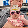Jaclyn is registered to the contest to win money with this photo: baby, man, glasses, pink_sunglasses, grocery_store, shopping, holding, casual_clothing, baby_clothing, striped_shirt, strawberry_patch, tattoo, indoor, adult, child, portrait, shopping_aisle, product_tag, supermarket, funny