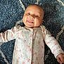 Vivienne is registered to the contest to win money with this photo: baby, smiling, infant, onesie, floral_pattern, blue_rug, lying_down, cute, tongue_out, happy, child, soft_texture, indoors, cozy, face, person, apparel, young, sleepwear, comfort