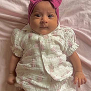 Selena is registered to the contest to win money with this photo: baby, infant, child, pink, headband, bow, blanket, clothing, cute, lying_down, portrait, indoors, soft_texture, white_outfit, patterned_clothing, small_hands, wide_eyes, adorable, pajamas, sleepwear