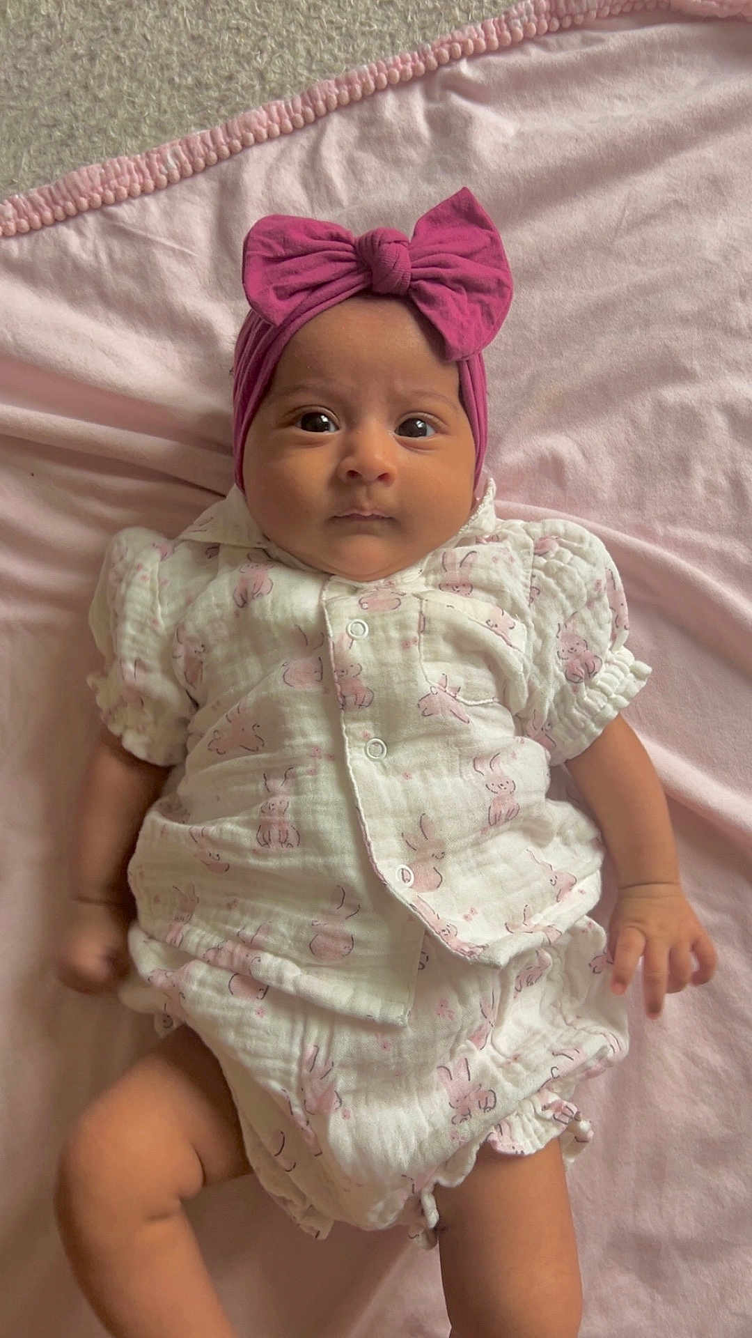 Selena is registered to the contest to win money with this photo: baby, infant, child, pink, headband, bow, blanket, clothing, cute, lying_down, portrait, indoors, soft_texture, white_outfit, patterned_clothing, small_hands, wide_eyes, adorable, pajamas, sleepwear