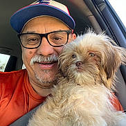 Molcha joined the competition — help win amazing prizes! man, dog, glasses, hat, car, seatbelt, orange_shirt, smiling, portrait, pet, fluffy_dog, window, interior, companion, casual, beard, mustache, daylight, close_up, happy