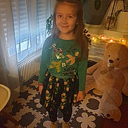 Natalia participe au concours pour gagner de l'argent avec cette photo : boots, child, cozy, curtains, fairy_lights, floral_skirt, girl, green_sweater, home, indoor, long_hair, patterned_floor, play_mat, portrait, potted_plants, radiator, smiling, standing, teddy_bear, warm_lighting