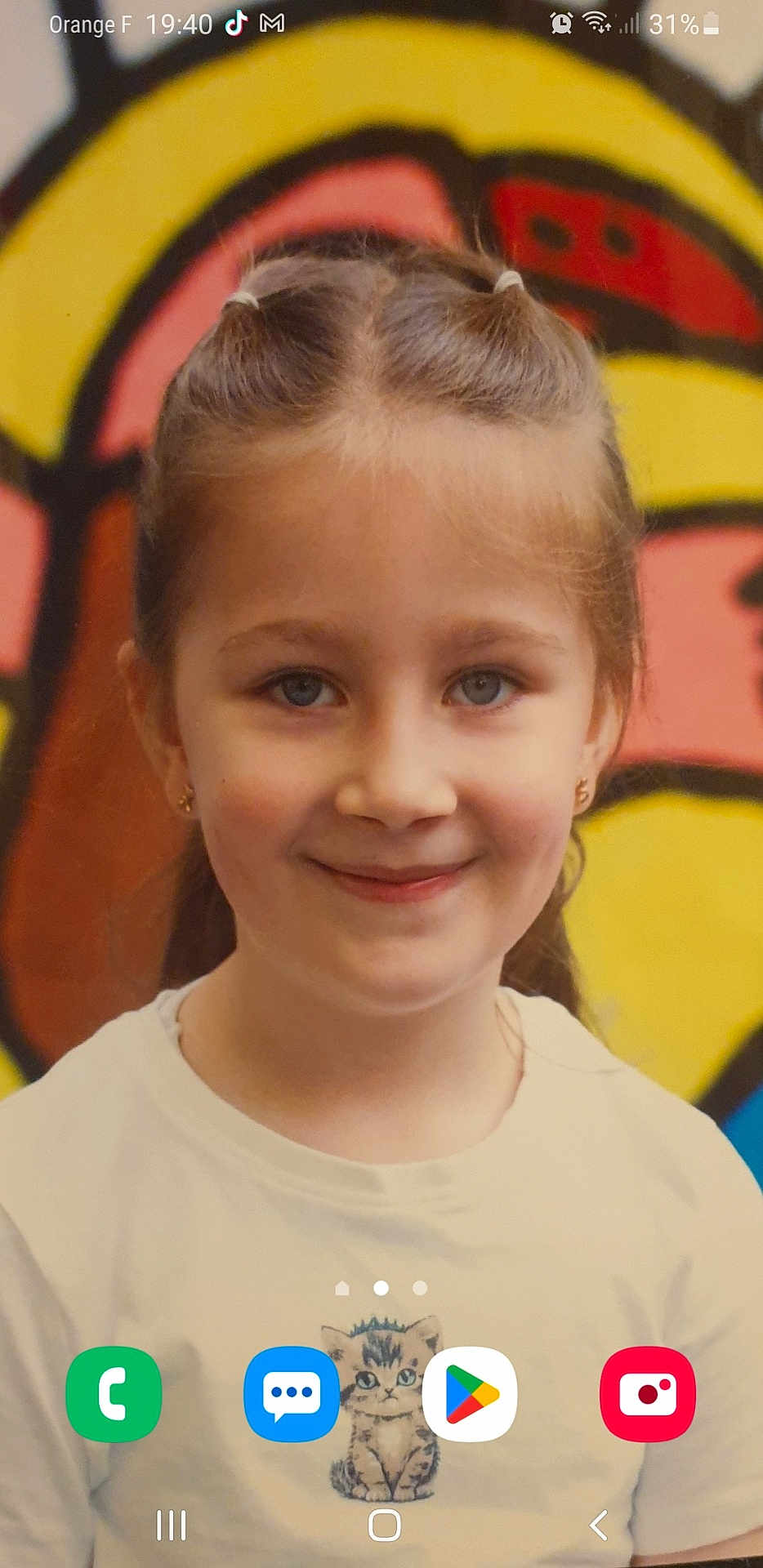 Emilija a rejoint le concours — aidez-le/la à gagner de superbes lots ! child, girl, smiling, braids, white_tshirt, kitten_print, graffiti, colorful_background, portrait, face, earrings, blue_eyes, phone_screenshot, app_icons, status_bar, casual_clothing, indoors, young_person, headshot, happy