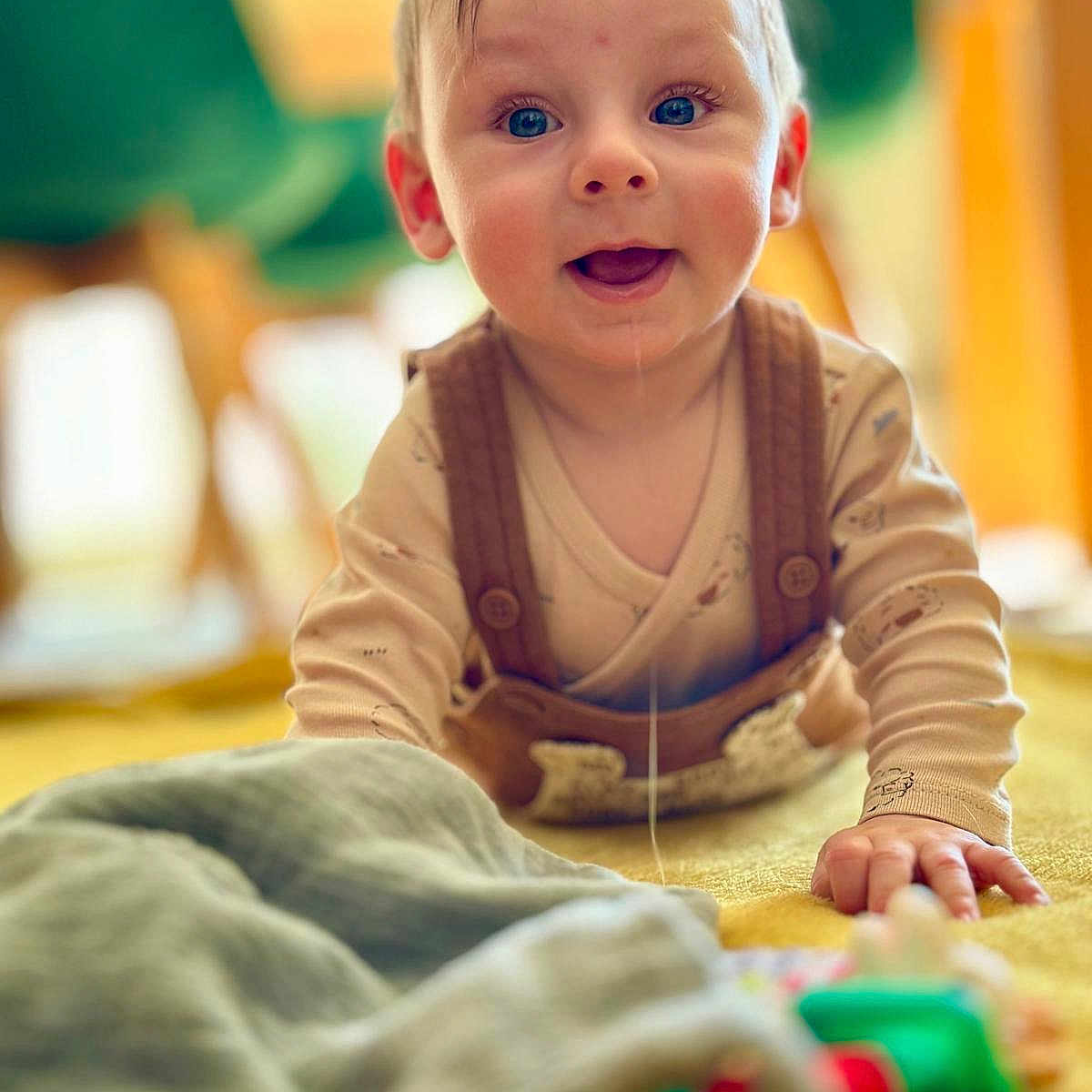Lissandro participe au concours pour gagner de l'argent avec cette photo : baby, child, crawling, drool, blue_eyes, brown_overalls, beige_shirt, blanket, toy, indoors, happy, cute, portrait, infant, playing, smiling, warm_colors, soft_focus, floor, young