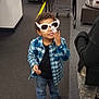 child, sunglasses, store, shopping_cart, plaid_shirt, blue_jeans, black_shoes, price_tag, carpeted_floor, clothing, rack, jacket, adult, shopping, retail, smiling, curly_hair, indoor, person, casual_wear