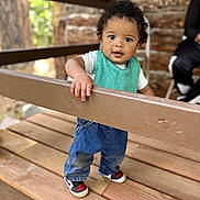 Justice joined the competition — help win amazing prizes! toddler, child, curly_hair, blue_jeans, sneakers, teal_bib, wooden_deck, railing, outdoor, person, curious_expression, hand, fence, portrait, daylight, casual_clothing, nature_background, blurred_background, standing, baby