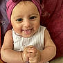 baby, child, infant, pink_bow, headband, smiling, tongue_out, clasped_hands, light_pink_clothing, blanket, embroidered_blanket, cute, happy, portrait, close_up, indoors, playful, person, skin, face