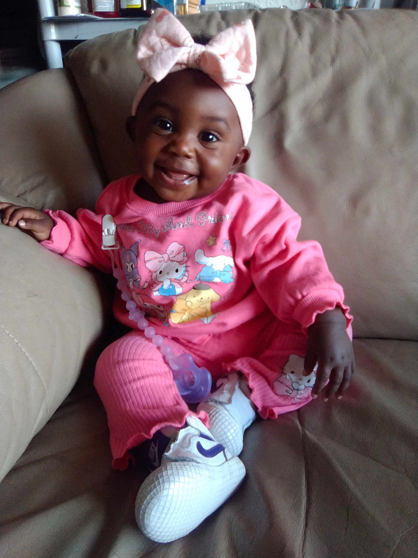 So'Lana joined the competition — help win amazing prizes! baby, child, smiling, pink_clothing, headband, bow, pacifier, couch, indoor, happy, sitting, footwear, sneakers, person, infant, cute, portrait, cozy, home, comfortable