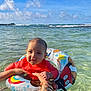 baby, child, inflatable_ring, ocean, water, tattoos, bracelets, sky, clouds, waves, red_shirt, swimming, summer, beach, sunlight, outdoor, cute, holding, person, fun