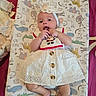 animal_print, baby, bib, bow, buttons, changing_mat, child, fingers, hands, happy, infant, lying_down, nursery, outdoorless, photography, playful, portrait, smiling, textile, white_dress