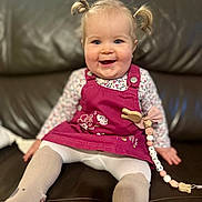 Alice participe au concours pour gagner de l'argent avec cette photo : baby, child, pigtails, pink_dress, floral_shirt, white_tights, smile, sitting, couch, leather, indoor, cute, happy, toddler, face, person, home, toy, accessory, clothing