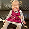 baby, child, pigtails, pink_dress, floral_shirt, white_tights, smile, sitting, couch, leather, indoor, cute, happy, toddler, face, person, home, toy, accessory, clothing