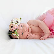 Maddison is registered to the contest to win money with this photo: baby, infant, flower_headband, pink_skirt, lying_down, soft_surface, cute, newborn, portrait, peaceful, skin, hand, face, head, eyes, expression, tulle, white_background, adorable, resting
