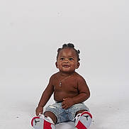 Christopher is registered to the contest to win money with this photo: toddler, child, sitting, smiling, denim_shorts, sneakers, studio, white_background, necklace, bare_chest, cute, happy, portrait, footwear, casual, young_child, black_hair, fashion, isolated, playful