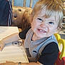 toddler, child, smiling, high_chair, restaurant, table, bracelet, blonde_hair, short_sleeve, vest, indoor, wooden_decor, people, background, happy, cute, furniture, seat, person, casual