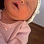 baby, newborn, infant, sleeping, hat, pink_clothing, closeup, portrait, rosy_cheeks, mouth_open, face, head, neck, hospital_bracelet, swaddle, soft_texture, indoor, wood_floor, peaceful, parent_arm