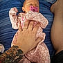 Harley is registered to the contest to win money with this photo: baby, newborn, pacifier, onesie, pink, floral_pattern, tattoo, adult_hand, blanket, striped, bed, sleeping, portrait, skin, leg, holding, closeup, infant, bedroom, cozy
