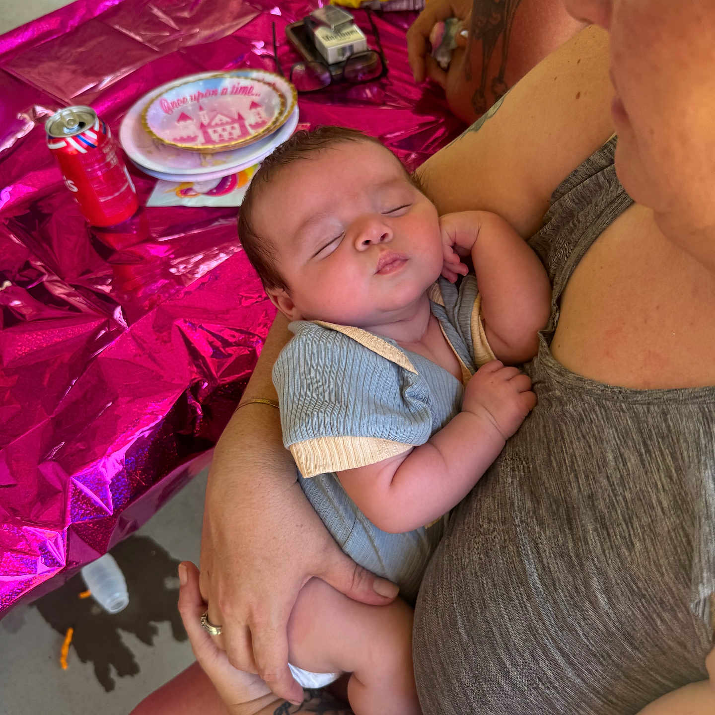 Taylyn is registered to the contest to win money with this photo: adult, arm, baby, casual, celebration, clothing, food, hand, indoor, infant, napkin, party, person, pink_wrapping, plate, sleeping, snacks, soda_can, table, tattoo