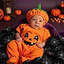 baby, pumpkin_costume, halloween, orange, purple, blanket, spiderweb, black, decorations, ghost, bat, pumpkin, candle, cute, indoors, portrait, child, holiday, festive, smiling