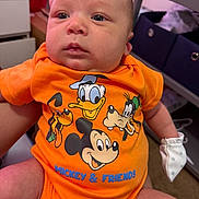 Liam joined the competition — help win amazing prizes! baby, infant, orange_clothing, mickey_mouse, donald_duck, goofy, pluto, onesie, mitten, person, indoor, furniture, storage_bins, dresser, carpet, cute, portrait, child, cartoon_characters, cute_baby