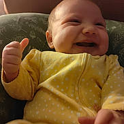 Kingsley is registered to the contest to win money with this photo: baby, smiling, thumbs_up, yellow_onesie, polka_dot, cushion, indoor, happy, infant, cute, child, portrait, closeup, soft_lighting, seated, clothing, person, young_child, expression, face