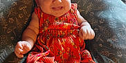 Kingsley is registered to the contest to win money with this photo: baby, child, smiling, dress, headband, indoor, cushion, pattern, happy, person, cute, infant, plush, seated, cheerful, portrait, colorful_clothing, young_child, soft_lighting, cozy