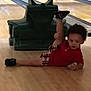 Michael joined the competition — help win amazing prizes! toddler, child, bowling_alley, bowling_pins, wooden_floor, ball_return, casual_clothing, red_shirt, plaid_shorts, black_shoes, indoor, recreation, playful, posing, floor, sports_equipment, lane, leisure, young_child, curly_hair